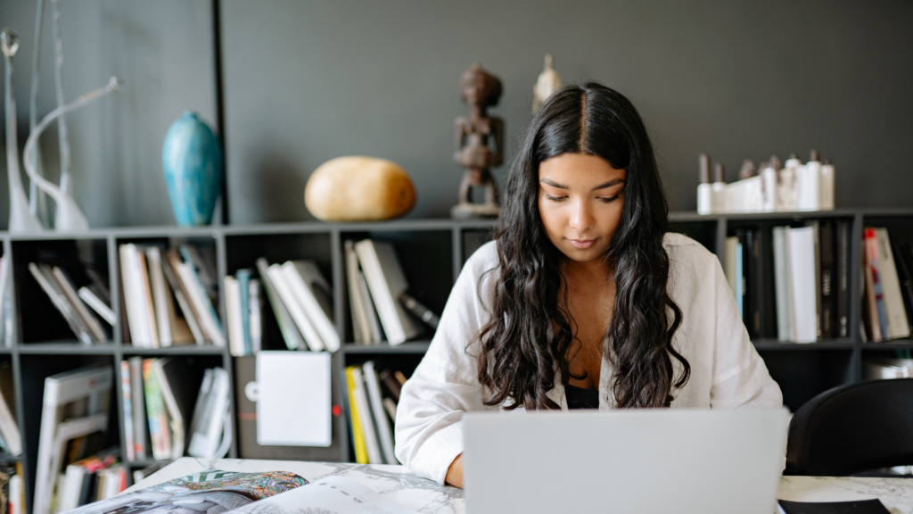 Woman on a laptop at home, reviewing dynamic pricing strategies for renting out her house as a photoshoot location, adjusting rates based on demand, seasonality, and availability to maximize income.